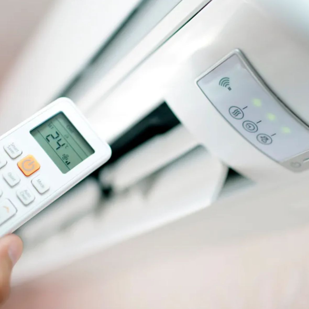 Mano sujeta control remoto frente a un aire acondicionado.