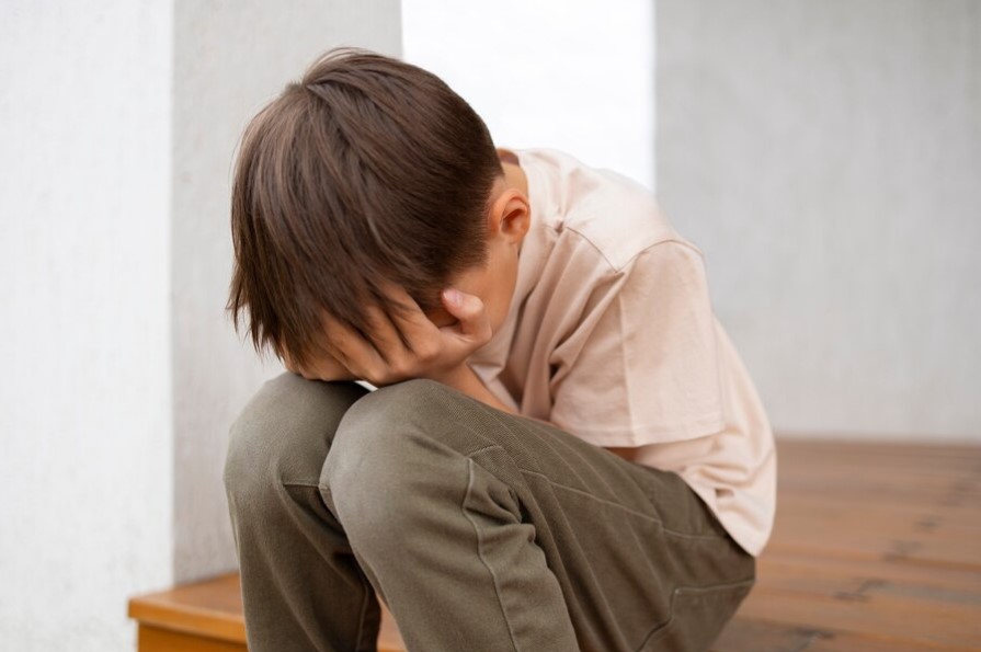 Ninño senyado, agarrandose la cara por tristeza