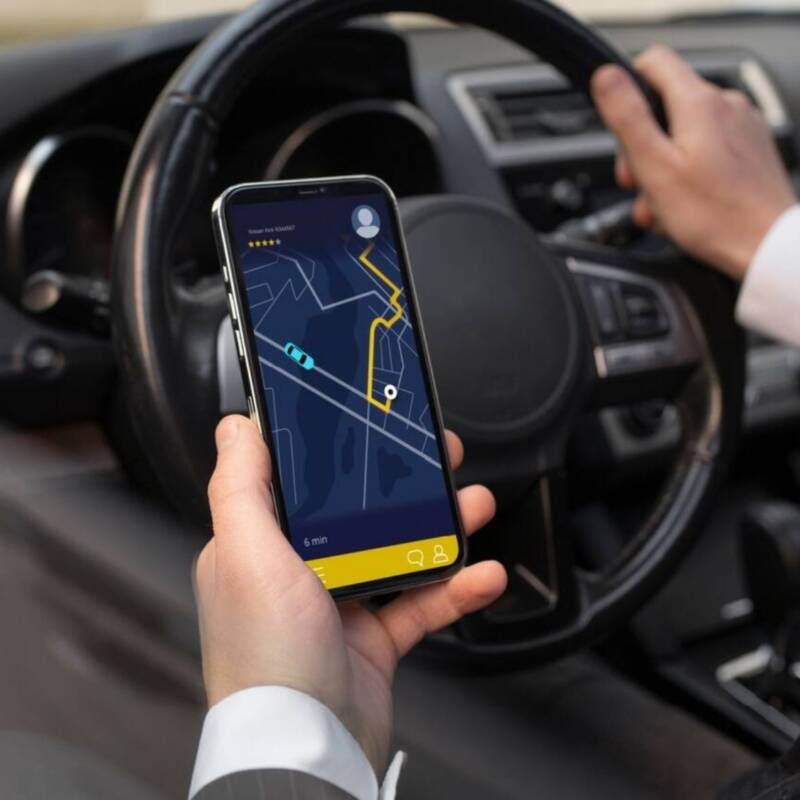 Plano detalle de conductor arriba del auto con su mano sosteniendo un dispositivo móvil con un mapa abierto.